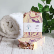 Load image into Gallery viewer, Two swirled soap bars with a label on a wooden surface, towel, and plant in the background.