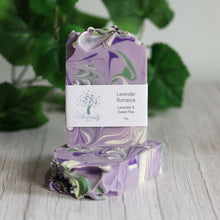 Load image into Gallery viewer, Purple and green marbled soap with a label on a wooden surface with green leaves in the background