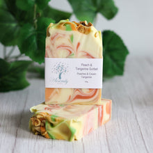 Load image into Gallery viewer, Colorful soap bar with a label on a light wooden surface with green leaves in the background