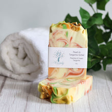 Load image into Gallery viewer, Stack of colorful soap bars with a visible brand label on a wooden surface.