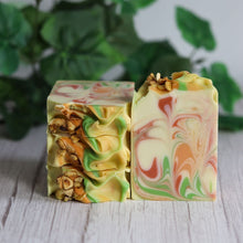 Load image into Gallery viewer, Two colorful soap bars with a marbled pattern on a wooden surface with green leaves in the background.