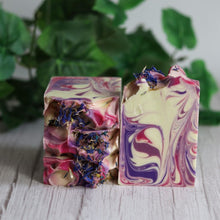Load image into Gallery viewer, Two colorful soap bars with floral elements on a wooden surface with a green leafy background.