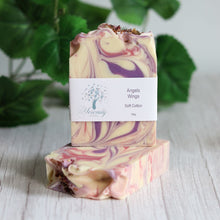 Load image into Gallery viewer, Marbled soap bars with a label on a wooden surface with green leaves in the background
