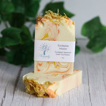 Load image into Gallery viewer, Marbled soap bar with a label on a wooden surface with green leaves in the background
