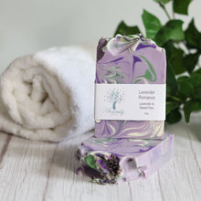 Load image into Gallery viewer, Lavender soap bar with a label on a wooden surface with a towel and plant in the background
