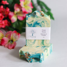 Load image into Gallery viewer, Marbled soap bar with 'Ocean Waves' label in front of flowers

