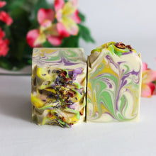 Load image into Gallery viewer, Two colorful soap bars with marbled patterns on a light surface, with flowers in the background.
