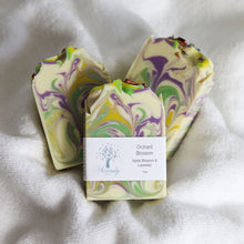 Load image into Gallery viewer, Three swirled soap bars with a label on a white fabric background
