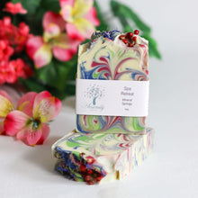 Load image into Gallery viewer, Colorful swirled soap with a label on a white surface with flowers in the background
